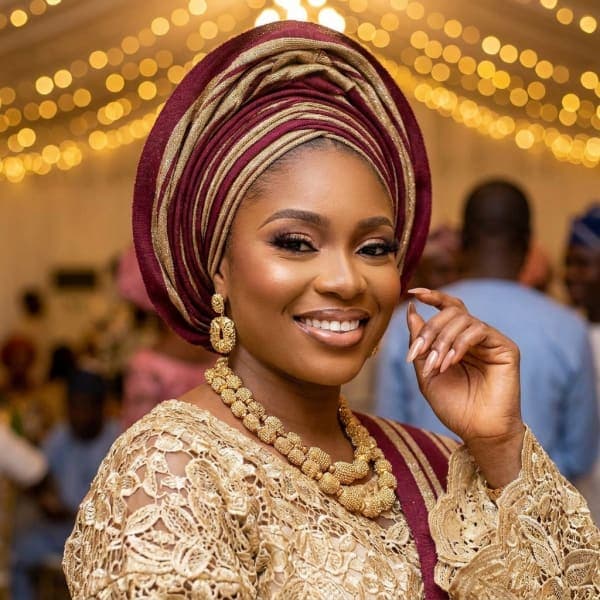 Owambe guest in a burgundy and gold gele with full glam makeup