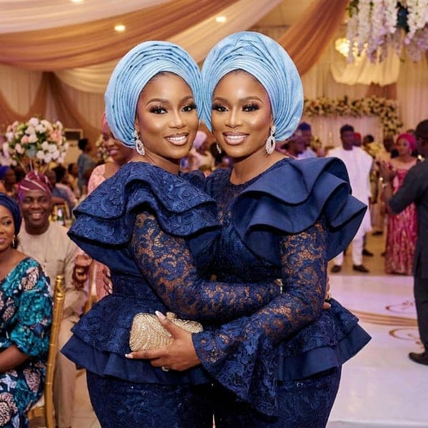 Two aso-ebi guests in navy lace with matching blue gele